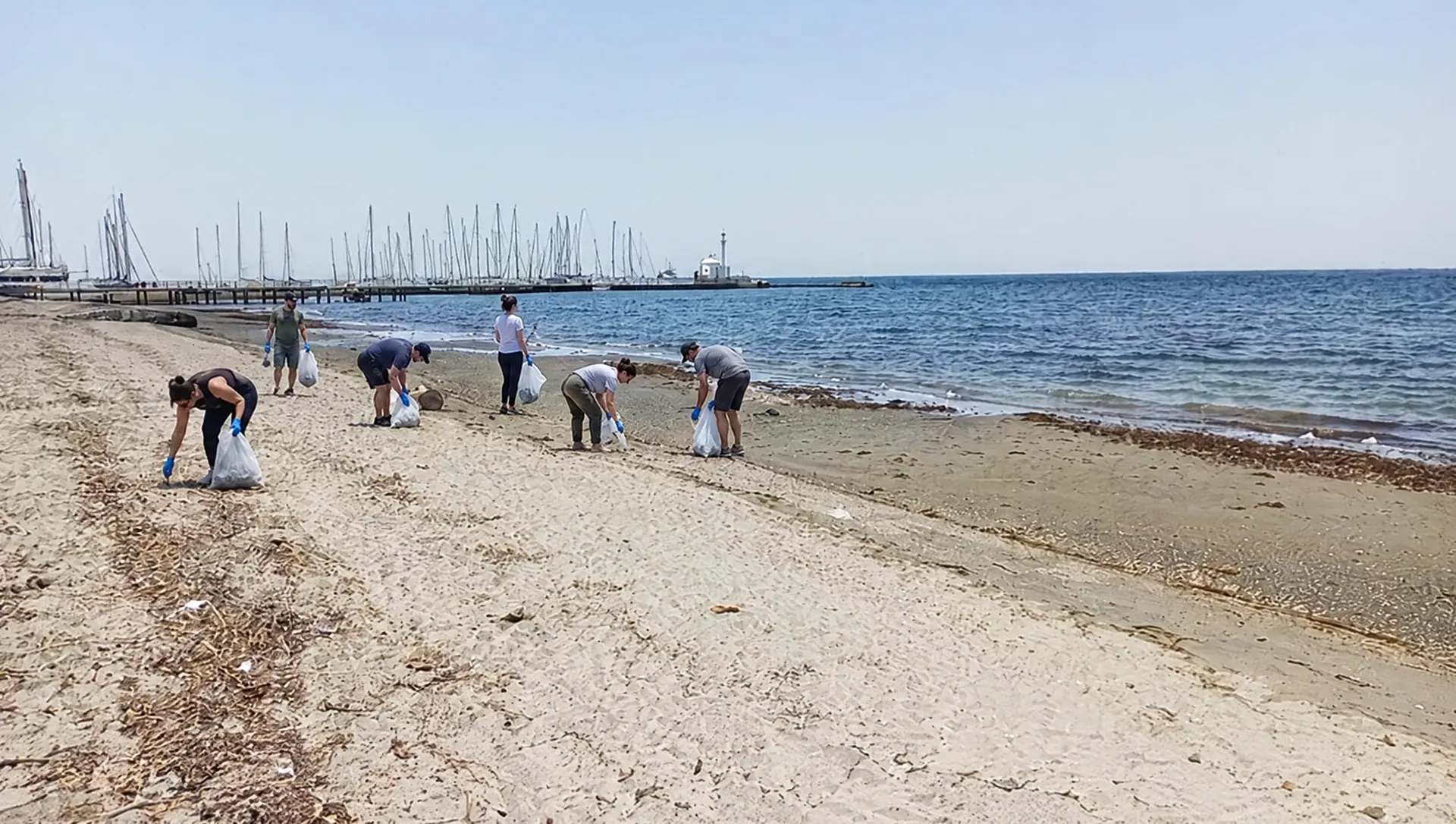 Εθελοντές στην άμμο με τη μαρίνα στο βάθος